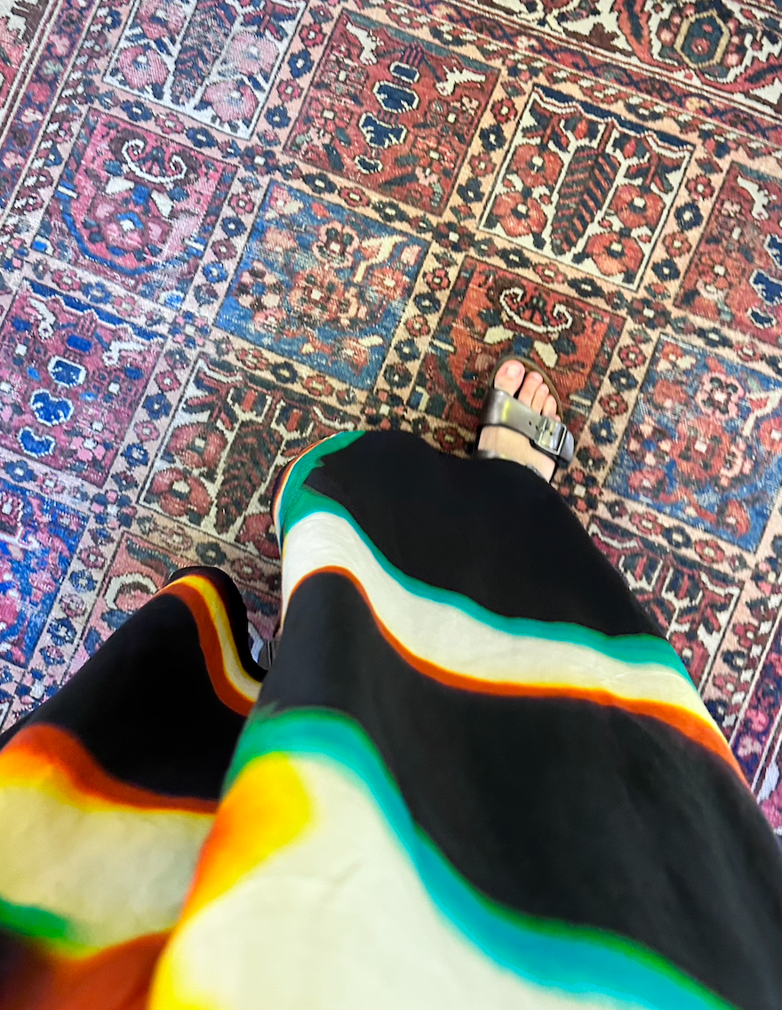 Vintage Persian Rug that is organic wool and has flowers and cypress tree in frames and color is red and blue or somehow pinkish a girl stand on it and wears a dress in an art store and wears BIRKENSTOCK sandals steps on Persian Vintage Rug 